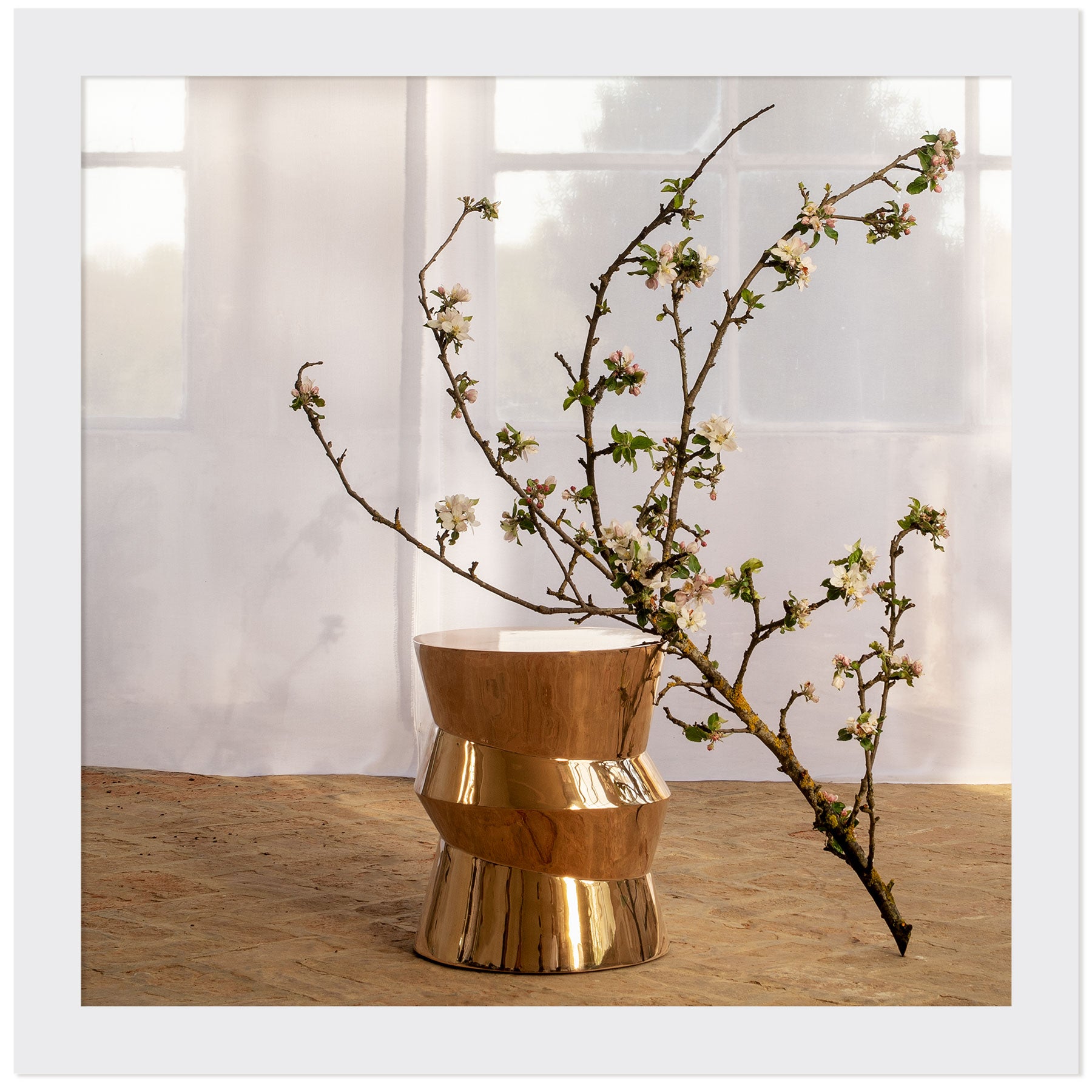Table d'appoint Dugo en bronze poli, une branche en fleur et un voilage en arrière plan